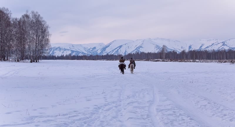 Two shepherd or cowboy riding a horse over the snowy mountains